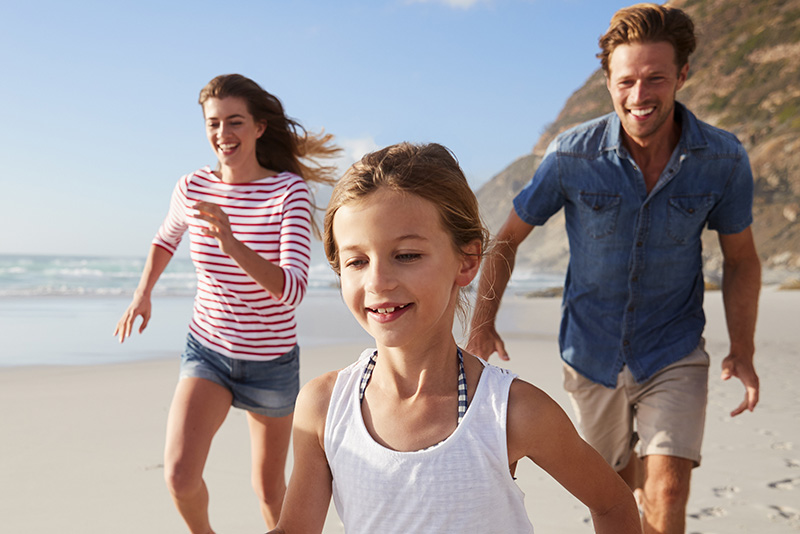 Two children and an adult running along a beach.
