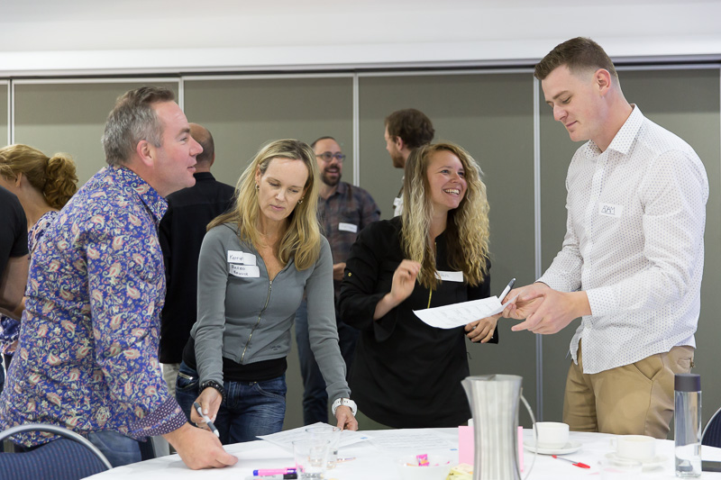 People around a meeting room table look at screens containing blocks of information.