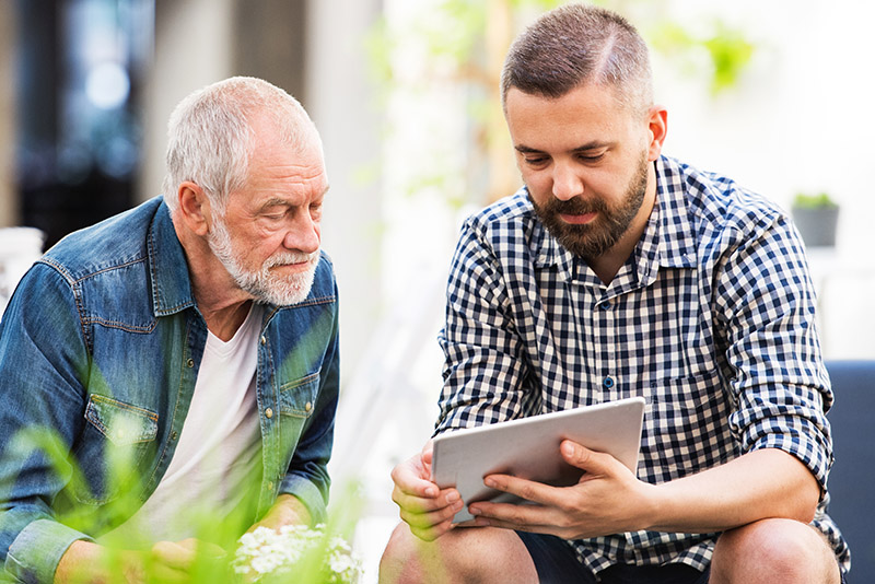 An older person and a younger person look at a device together.