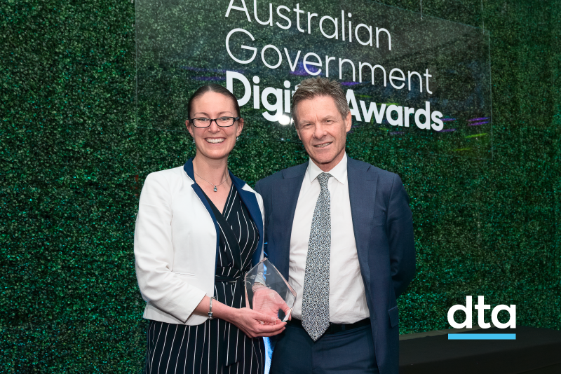 Two people in front of a plant wall. One is receiving an award.
