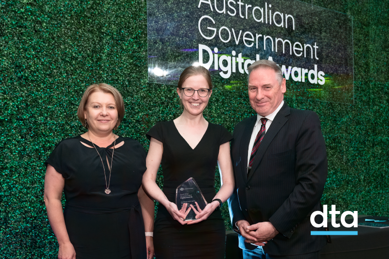 Three people standing in front of a plant wall receiving an award.
