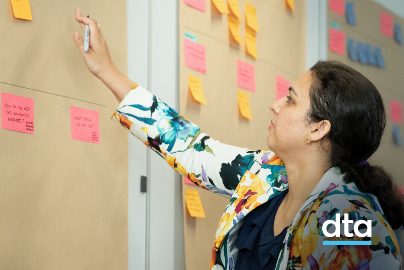 Person pointing to post-it note on the wall covered in butcher's paper
