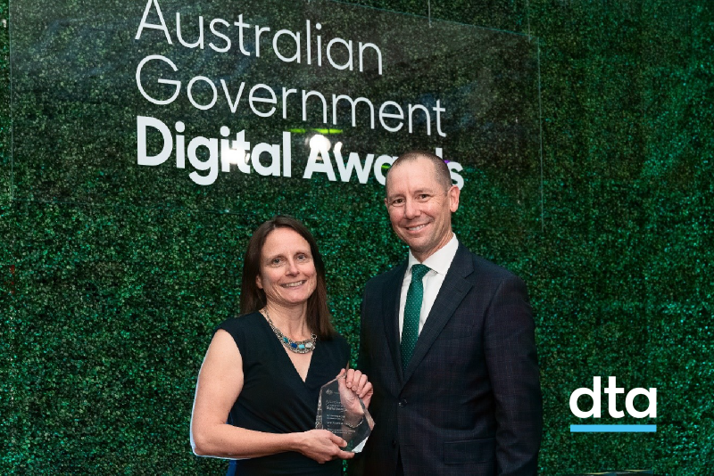 The CEO of the DTA and the winner of the award stand in front of a plant wall.